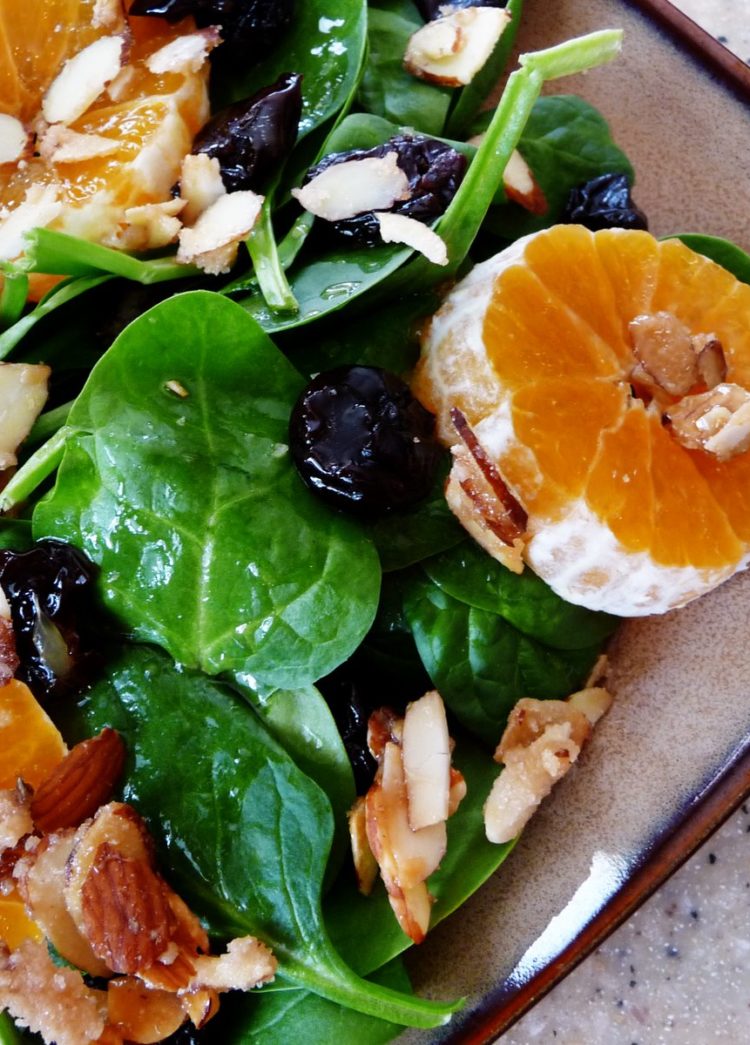 A vibrant spinach clementine salad on a rustic plate, featuring fresh baby spinach, juicy clementine slices, candied almonds, and dried cherries, all lightly dressed for a refreshing and flavorful dish