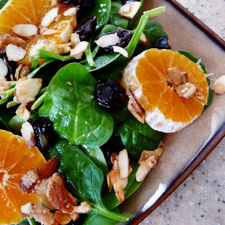 A vibrant spinach clementine salad on a rustic plate, featuring fresh baby spinach, juicy clementine slices, candied almonds, and dried cherries, all lightly dressed for a refreshing and flavorful dish