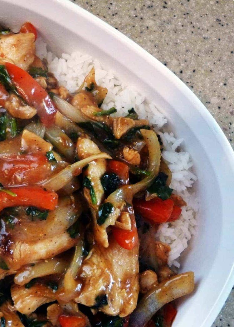 Chicken and pepper stir fry over rice on a white plate.