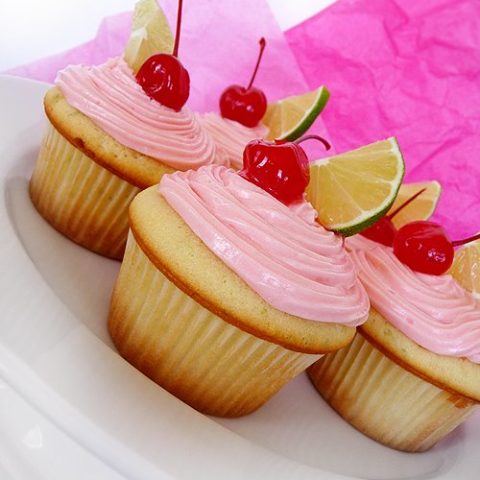 a plate of cherry limeade cupcakes frosted with maraschino cherry buttercream frosting and garnished with fresh lime slices