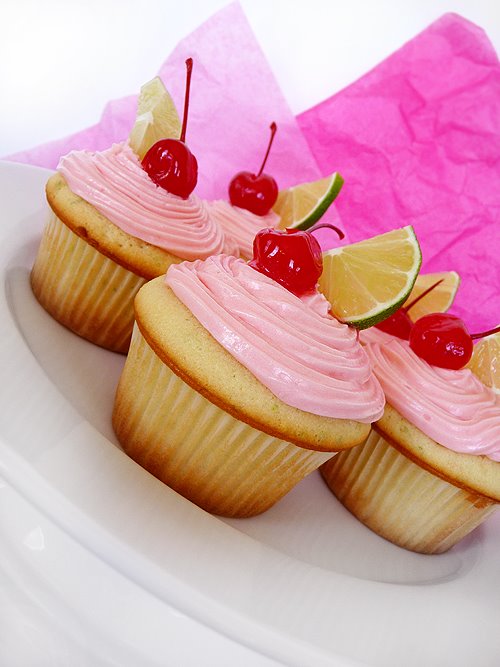 a plate of cherry limeade cupcakes frosted with maraschino cherry buttercream frosting and garnished with fresh lime slices