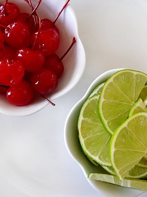 maraschino cherries and sliced limes in white bowls to be used for garnishing cherry limeade cupcakes