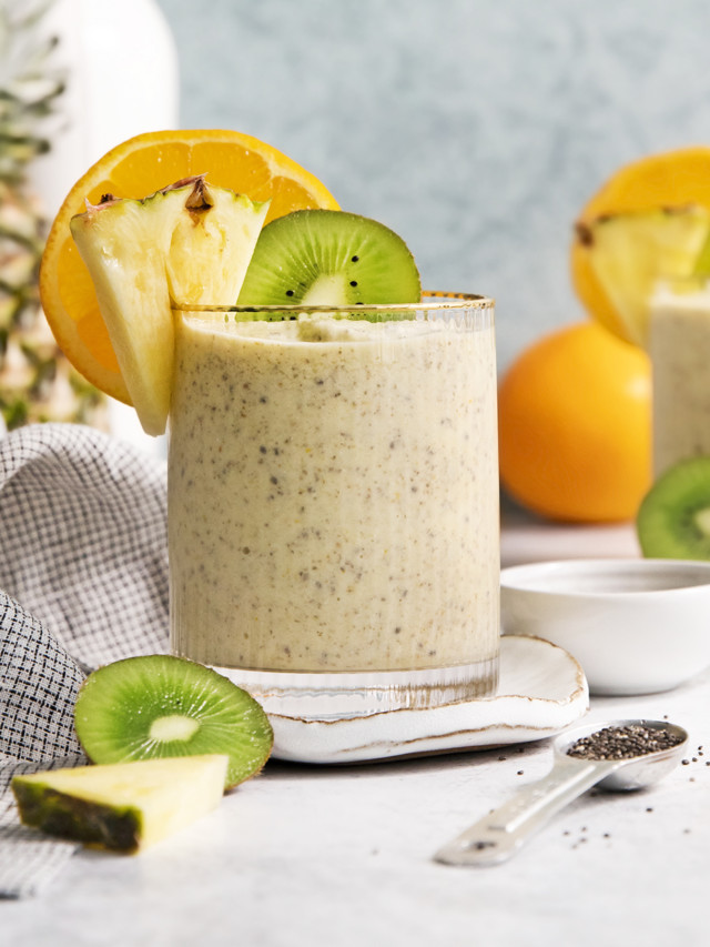 glass filled with a pineapple orange smoothie garnished with fresh orange, pineapple, and kiwi