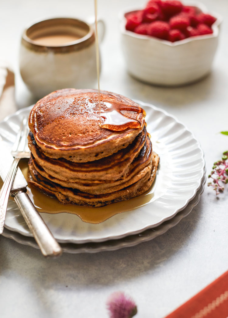 maple syrup drizzling on a plate of multigrain pancakes