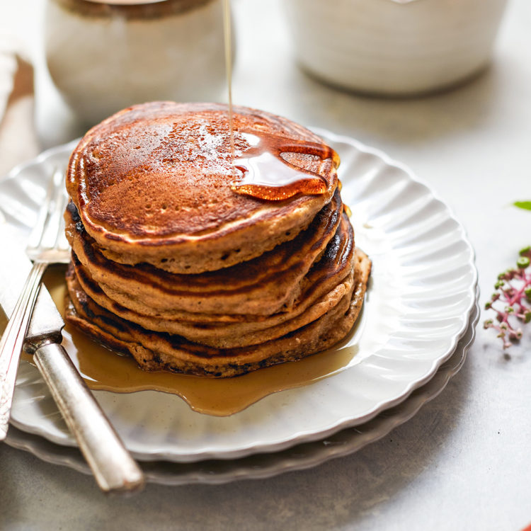 maple syrup drizzling on a plate of multigrain pancakes