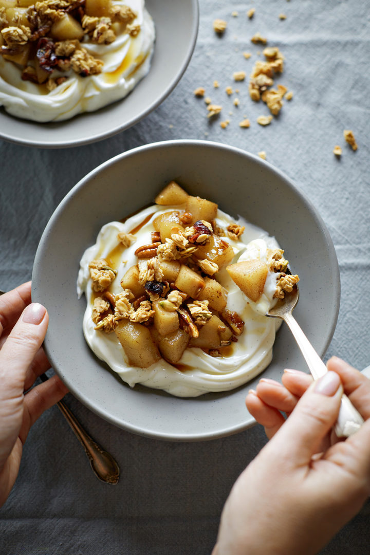 woman eating a bowl of yogurt with granola and spiced pear compote