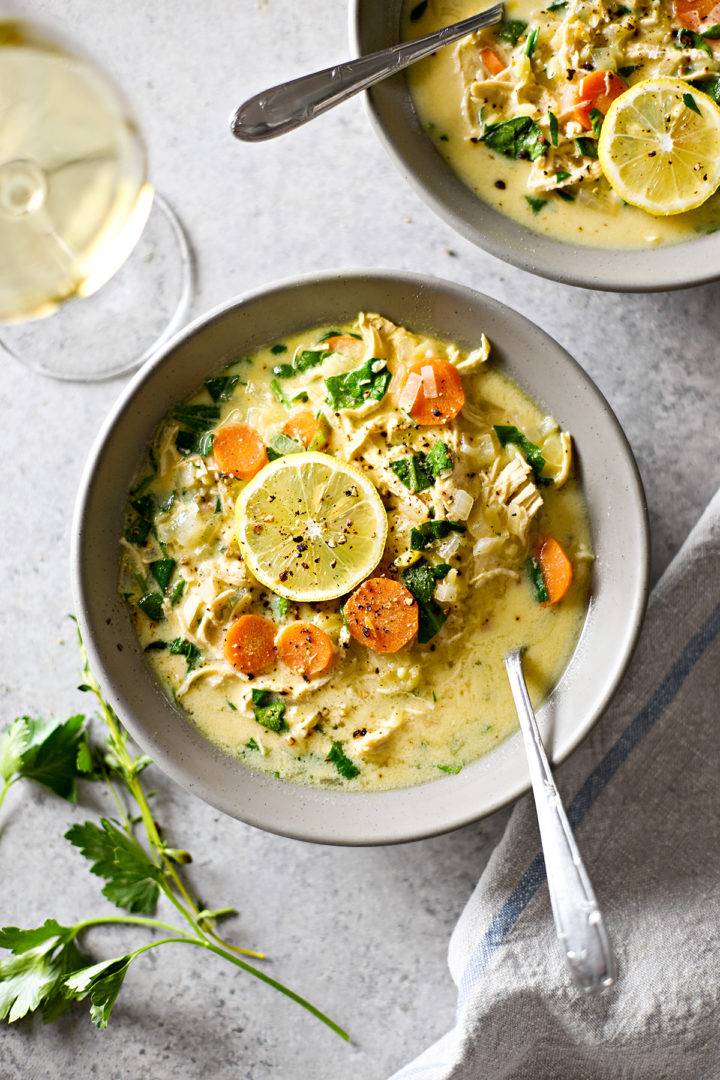 An overhead shot of a warm bowl of creamy chicken spinach orzo soup with fresh lemon slice garnishes.
