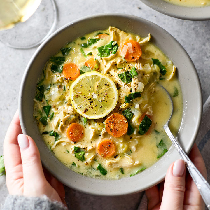 woman holding a bowl of lemon chicken orzo soup with spinach