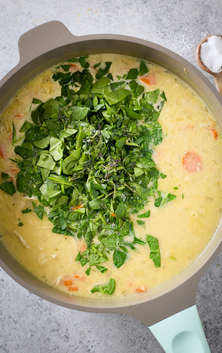 The final step of adding fresh spinach and herbs to chicken spinach orzo soup in a Dutch oven.