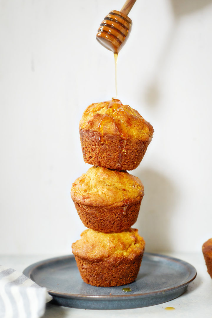 woman pouring honey on a honey cornbread muffin