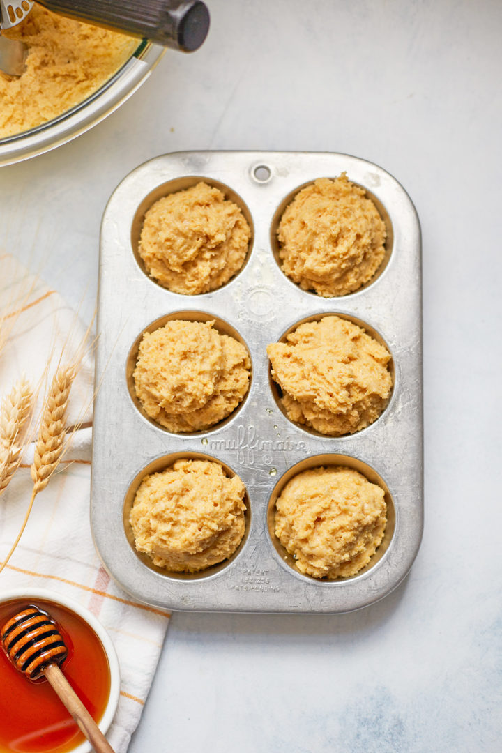 cornbread muffin batter in a muffin tin next to a bowl of honey