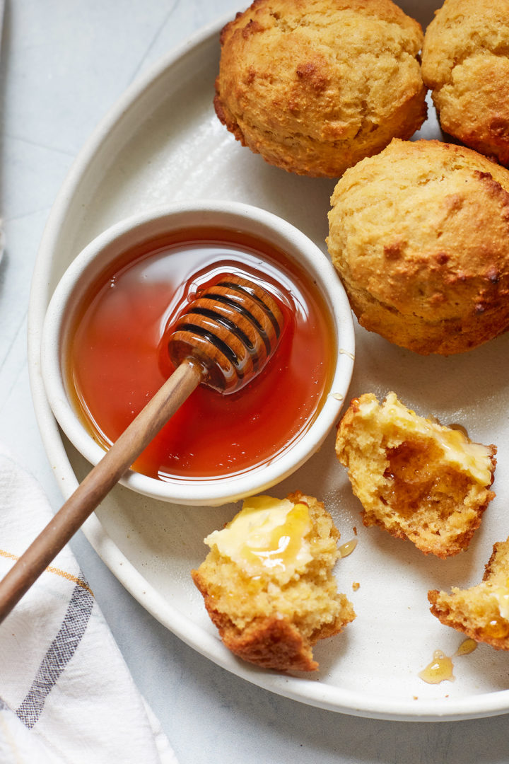 a plate of buttered cornbread muffins with a bowl of honey