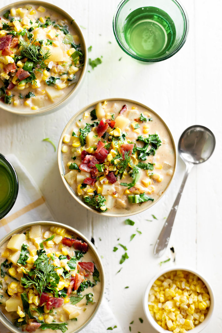 overhead view of three bowls of roasted corn chowder on a white wooden table