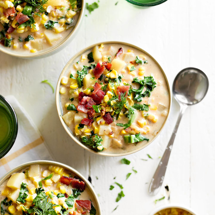 overhead view of three bowls of roasted corn chowder on a white wooden table