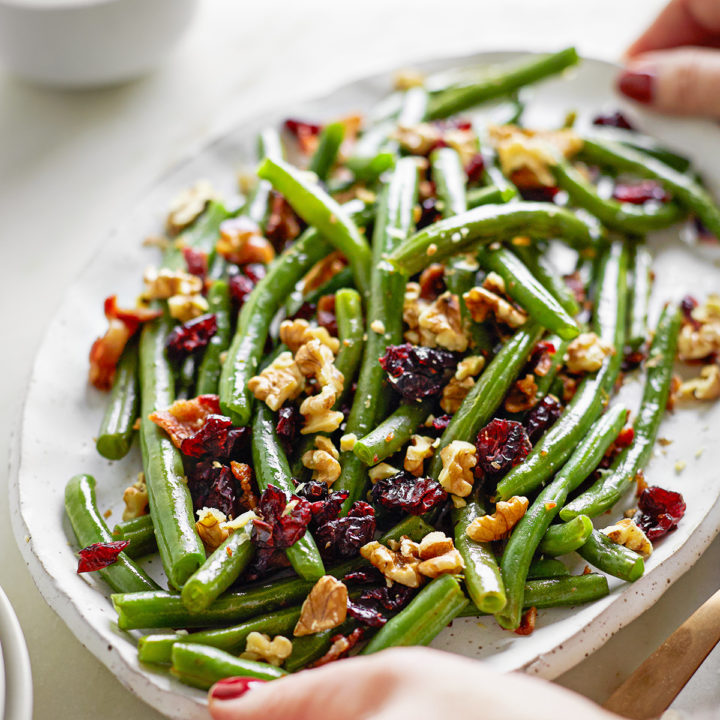 woman holding a serving plate of cranberry bacon green beans