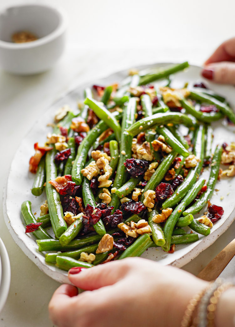 woman holding a serving plate of cranberry bacon green beans