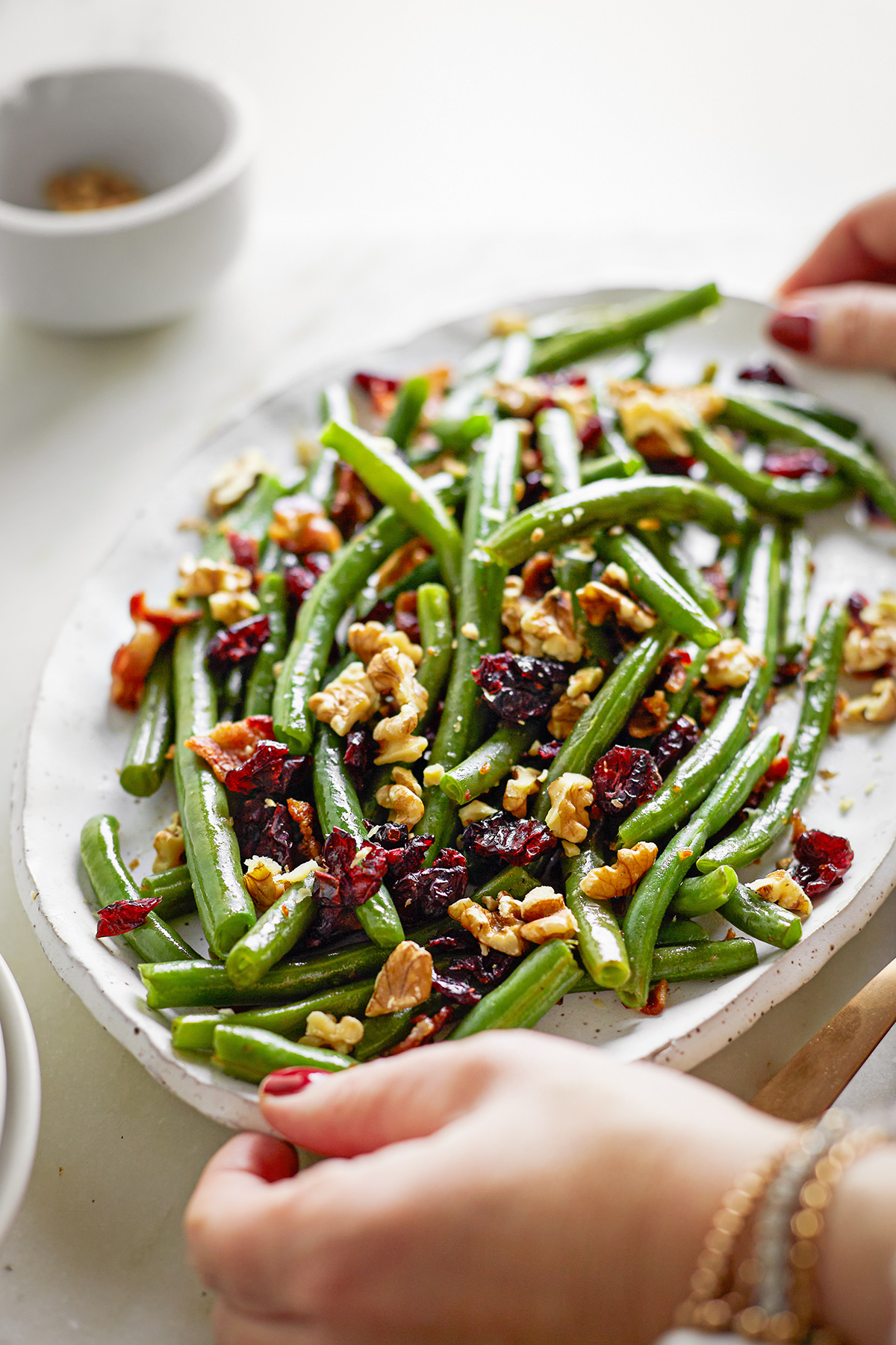 woman holding a serving plate of cranberry bacon green beans