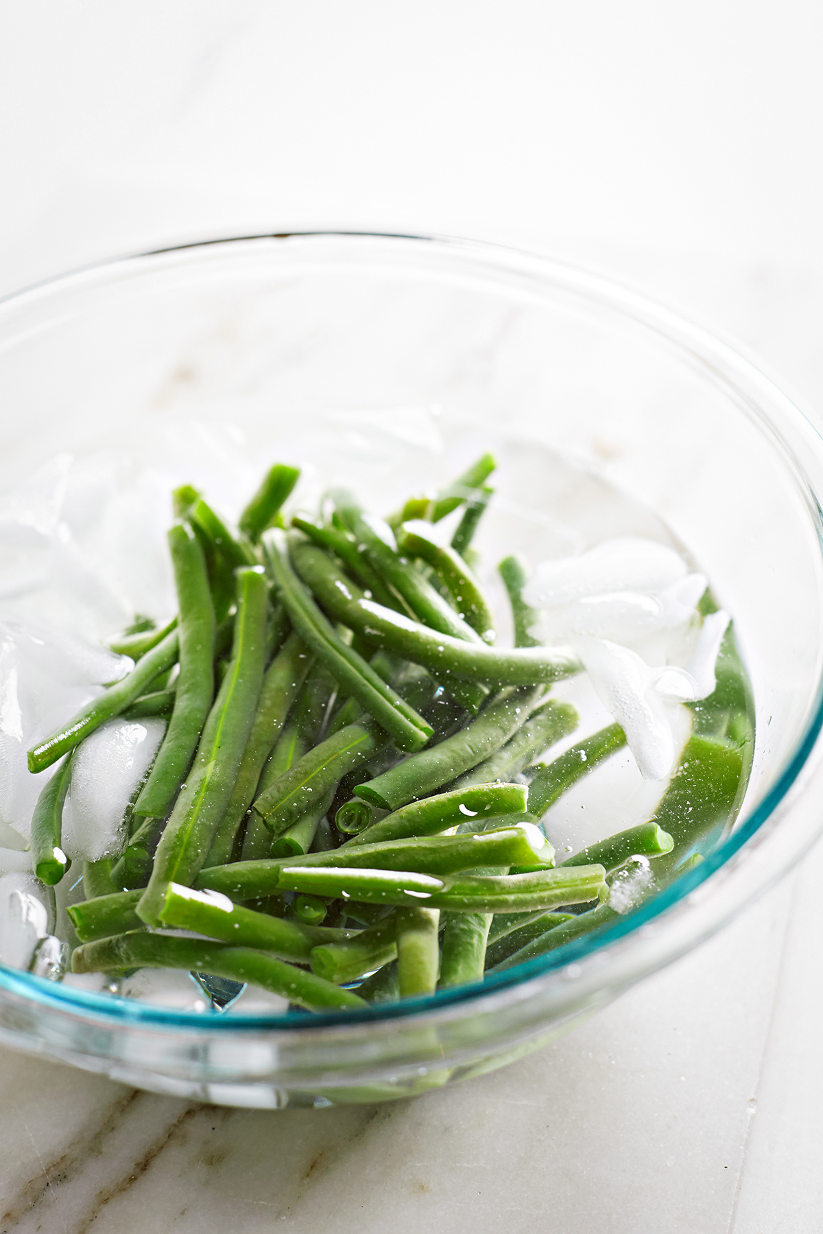 a bowl of green beans blanching in ice water