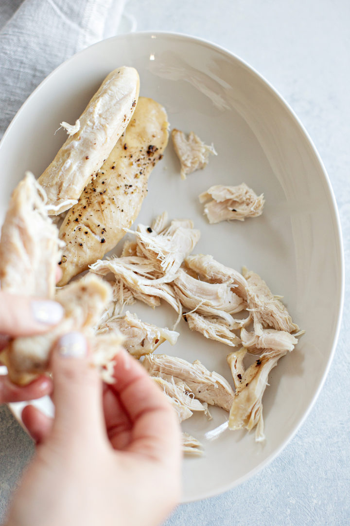 woman shredding chicken for chicken and chickpea curry soup