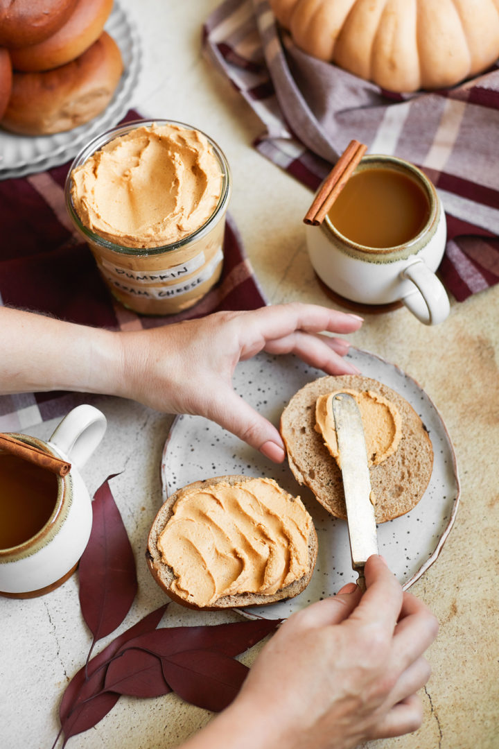 woman spreading pumpkin spice cream cheese on a bagel