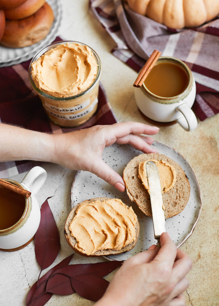 woman spreading pumpkin spice cream cheese on a bagel