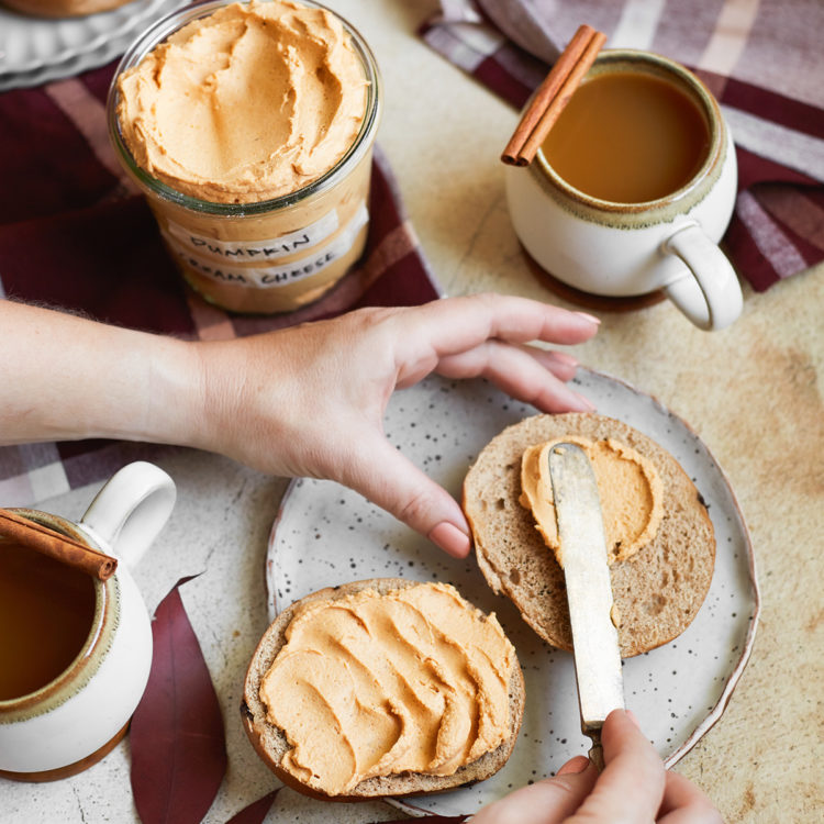 woman spreading pumpkin spice cream cheese on a bagel