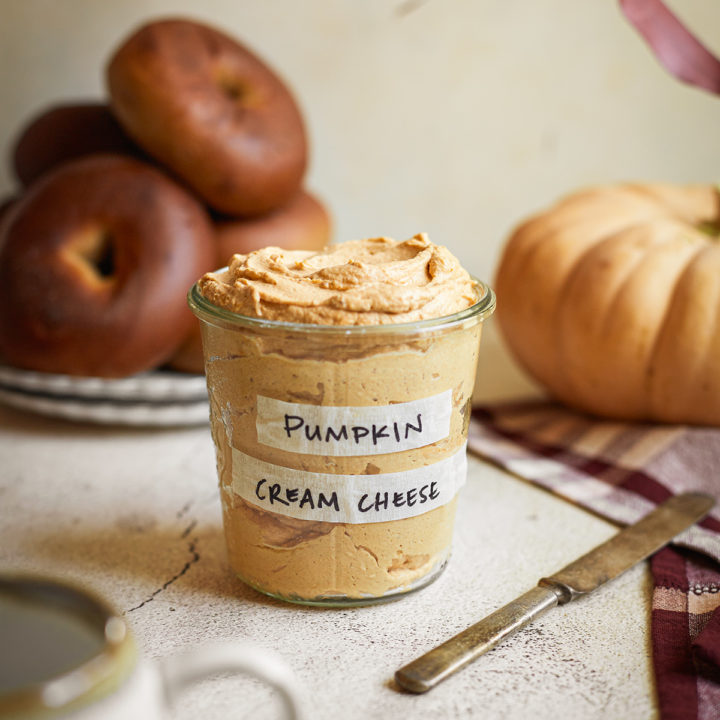 a jar of pumpkin cream cheese spread next to a plate of bagels