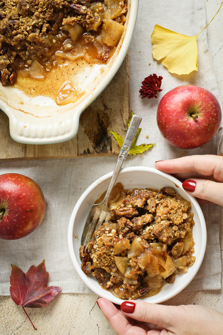 woman holding a bowl of bourbon apple crisp on a thanksgiving table  