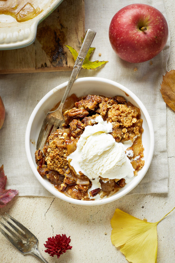 a bowl of brown butter bourbon apple crisp with vanilla ice cream