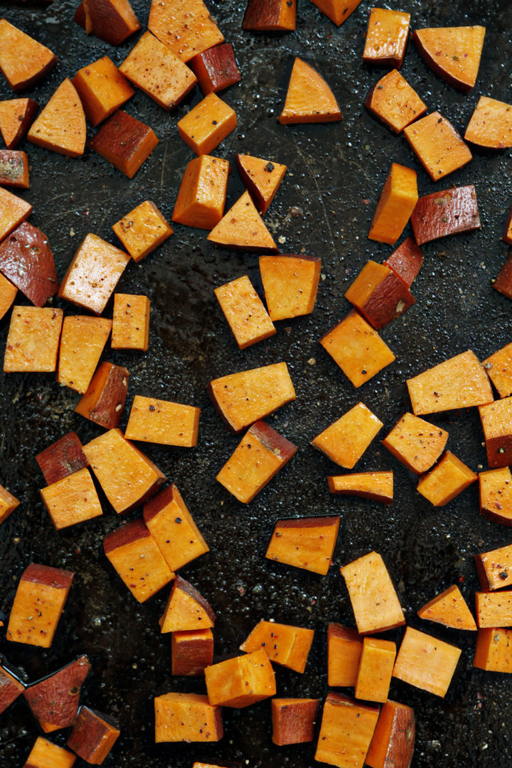 Cubed sweet potatoes tossed in olive oil, salt, and pepper, spread evenly on a baking sheet, ready to be roasted for the quinoa chicken salad.