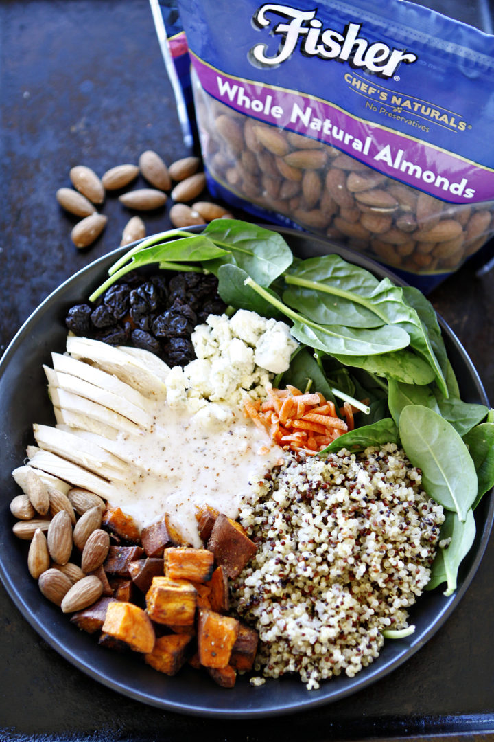 chicken and quinoa salad in a bowl, loaded with fresh spinach, roasted sweet potatoes, tender chicken, fluffy quinoa, blue cheese crumbles, dried cherries, and crunchy almonds, all topped with a creamy almond white balsamic dressing. A bag of almonds sits in the background