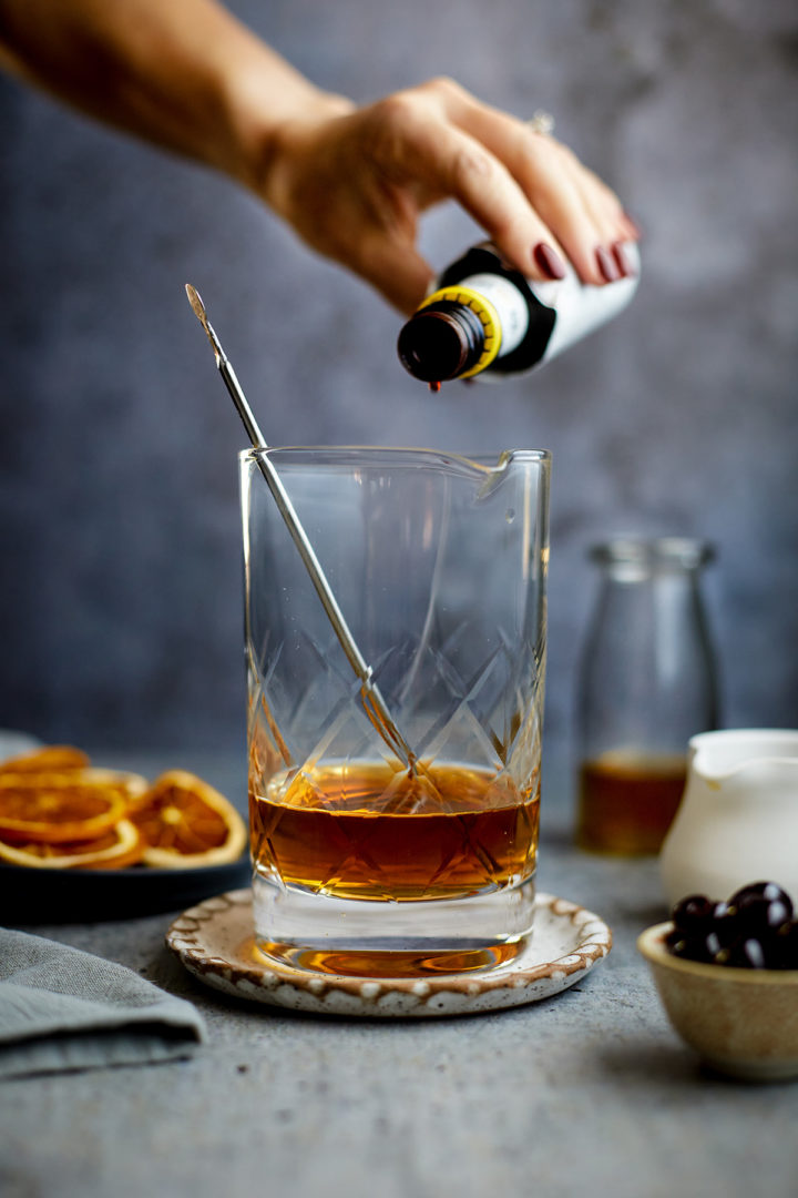 woman adding angostura bitters to an old fashioned