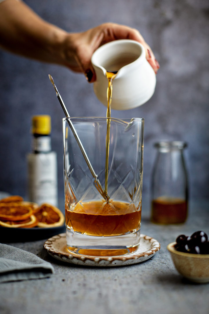 woman poouring bourbon into a cocktail mixing glass