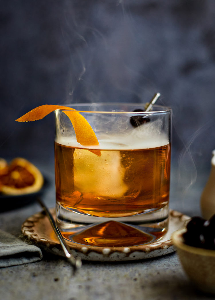 smoked old fashioned in a glass with orange and cherry garnish