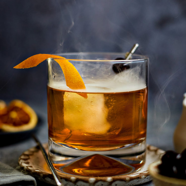 smoked old fashioned in a glass with orange and cherry garnish