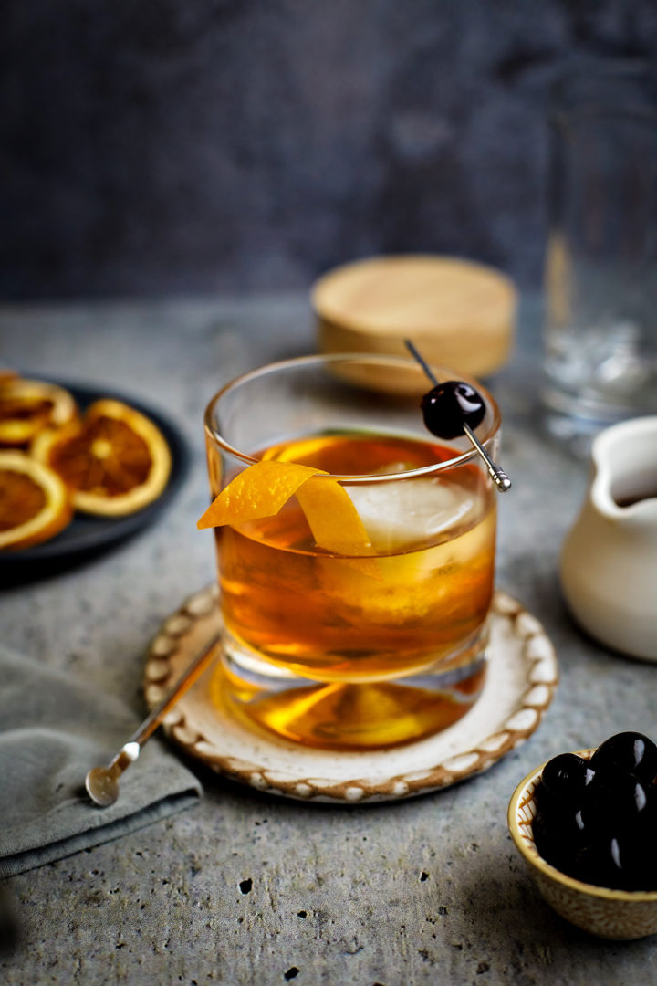 smoked old fashioned in a glass with an orange and cherry garnish