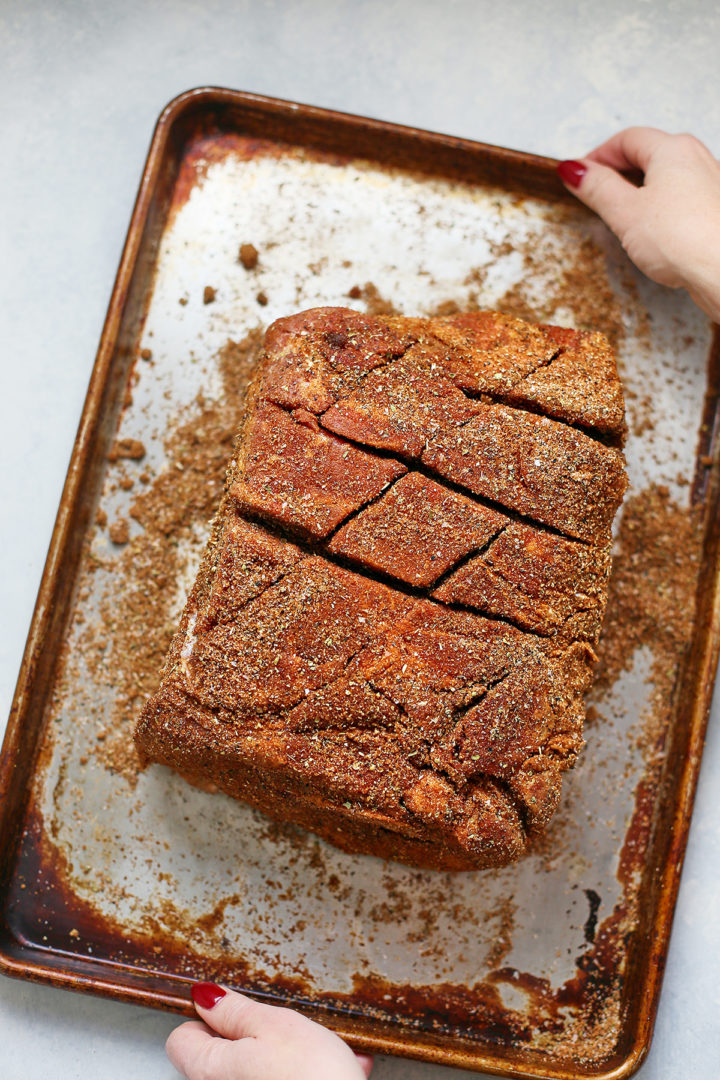 woman holding a tray with a seasoned pork shoulder on it