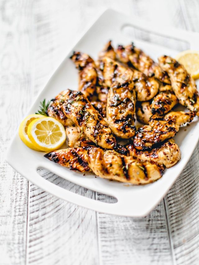 white platter with grilled glazed chicken tenderloins and lemon slices