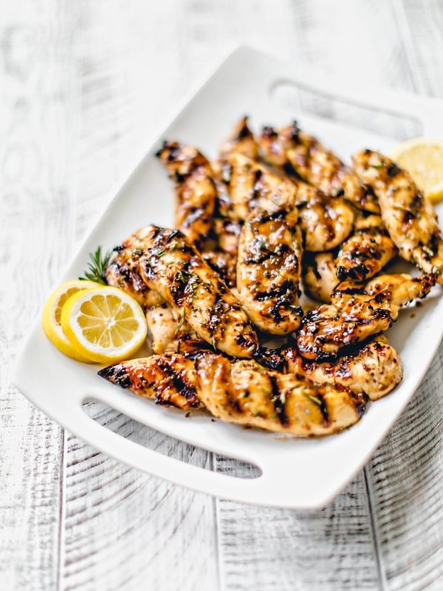 white platter with grilled glazed chicken tenderloins and lemon slices