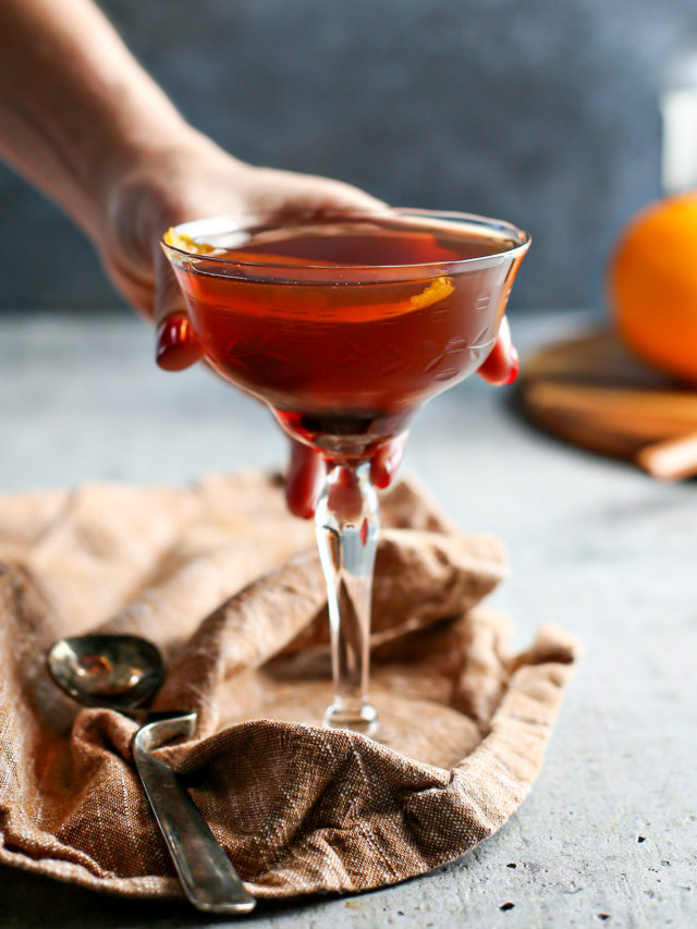 photo of a woman holding a black manhattan cocktail in a coupe glass