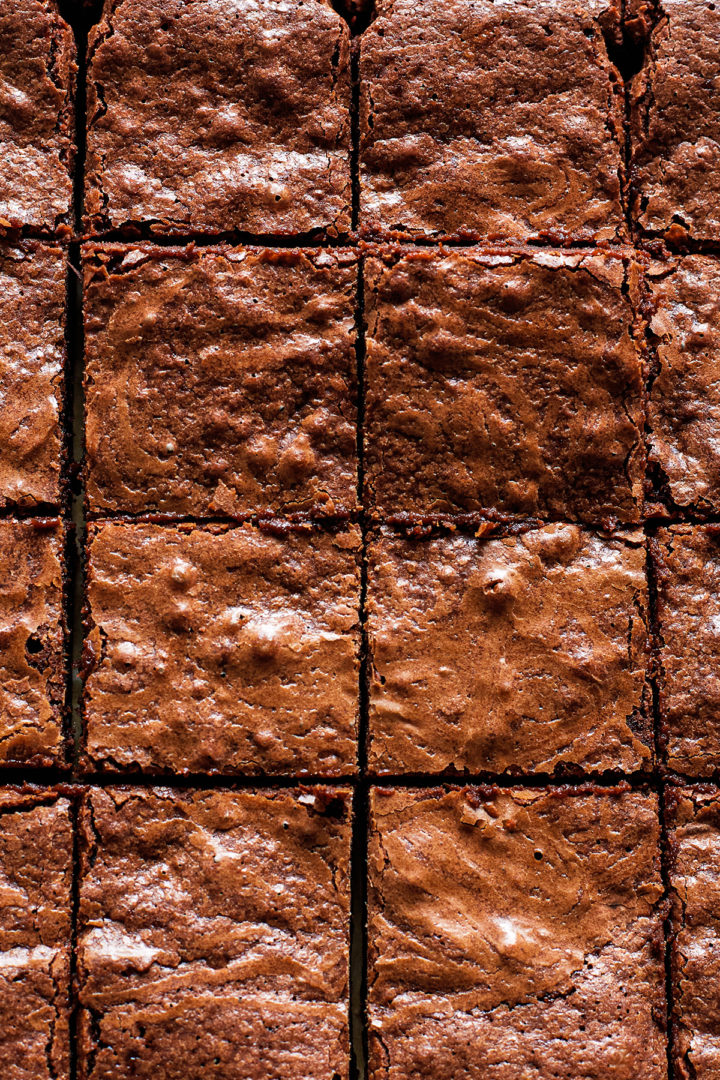 close up of a batch of freshly baked homemade brownies cut into squares, with a crackly top and fudgy texture.