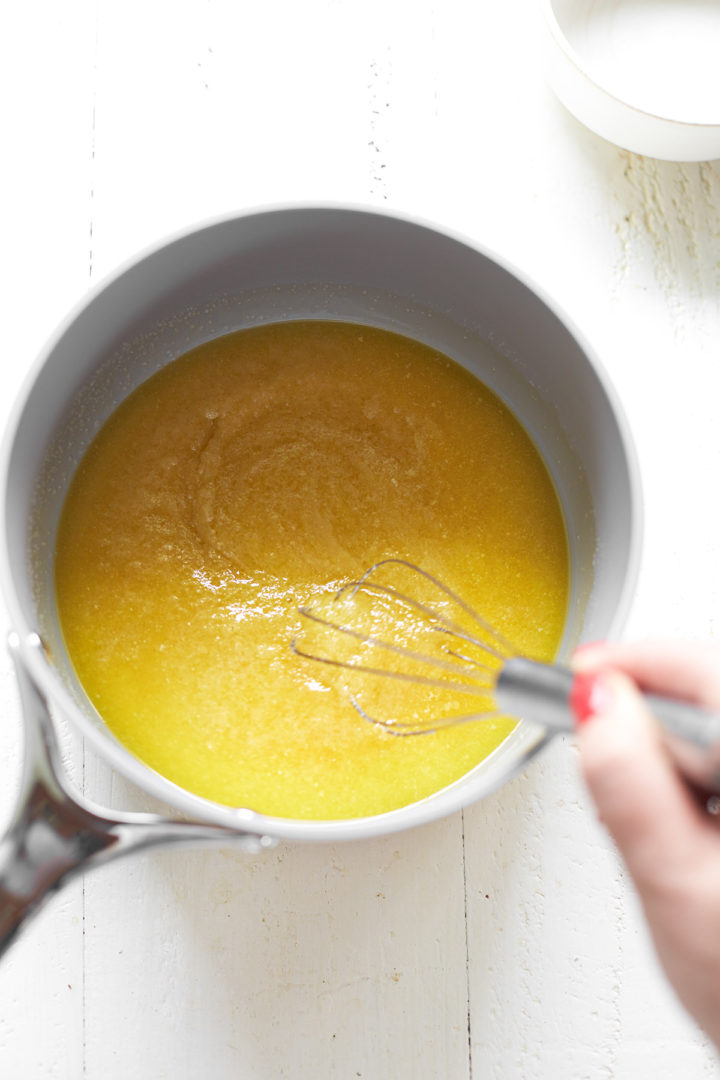 A woman stirring melted butter and sugar together in a mixing bowl to make homemade brownies.