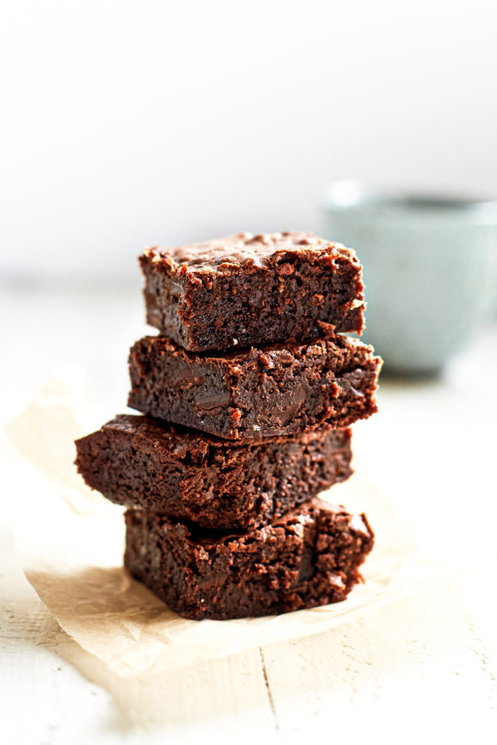 A stack of chewy fudge brownies on a piece of parchment paper, with a rich chocolatey texture.