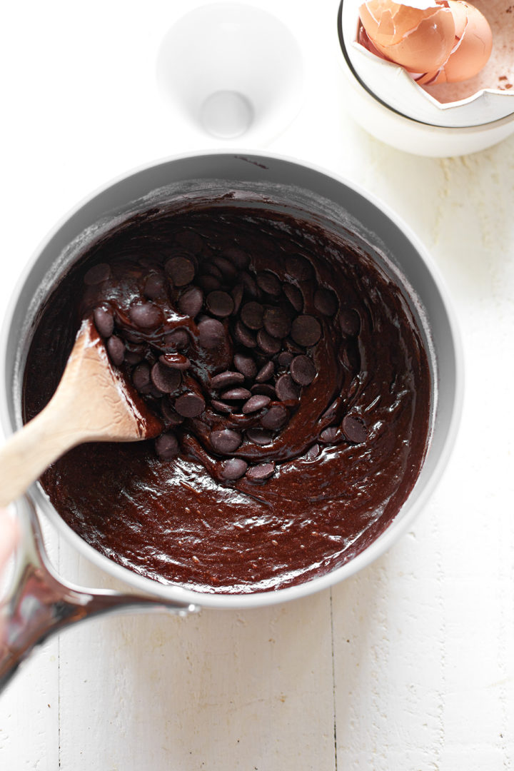 Chocolate chips being stirred into brownie batter with a wooden spoon.