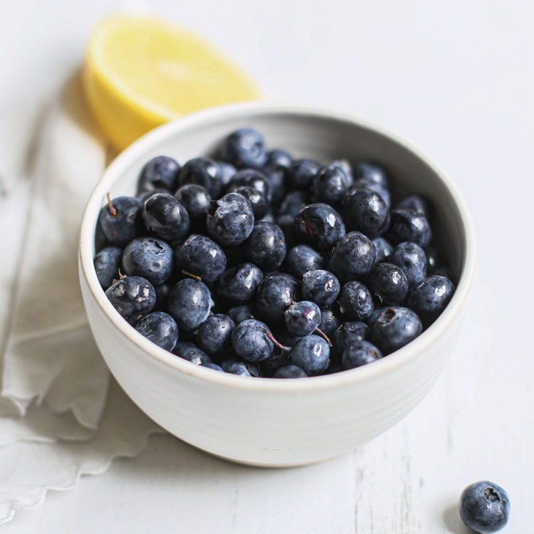 a bowl of fresh blueberries on a white wooden table before being frozen