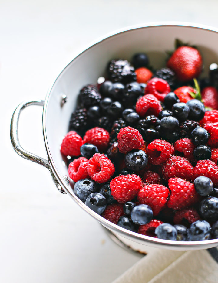 a white colander of fresh blueberries, raspberries, and blackberries after washing