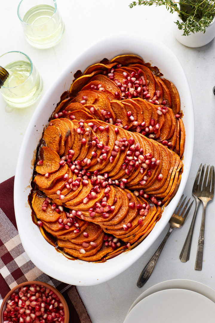 sliced sweet potato casserole topped with pomegrante in a white baking dish