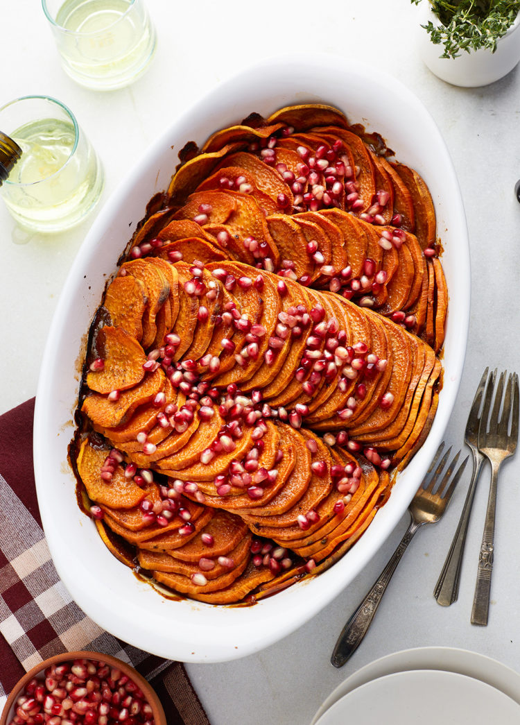 sliced sweet potato casserole topped with pomegrante in a white baking dish