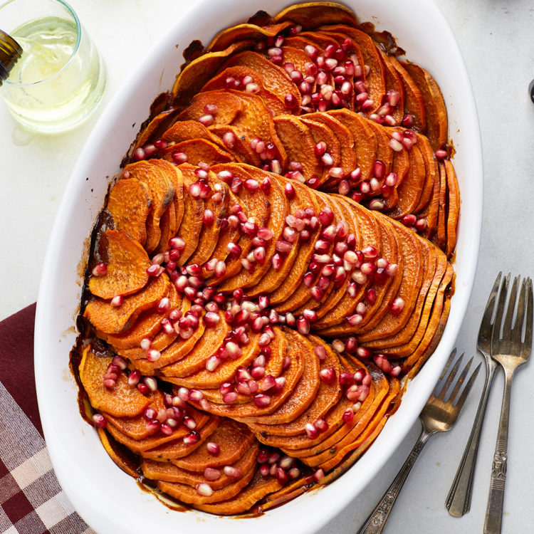 sliced sweet potato casserole topped with pomegrante in a white baking dish