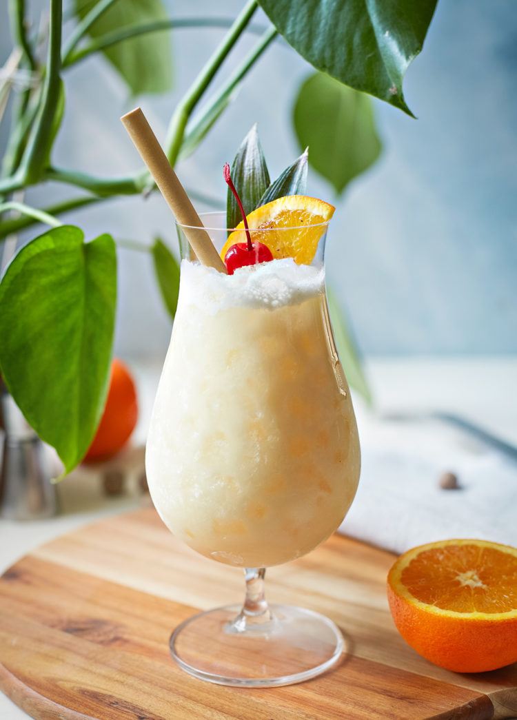 painkiller cocktail in a hurricane glass with orange and cherry garnish